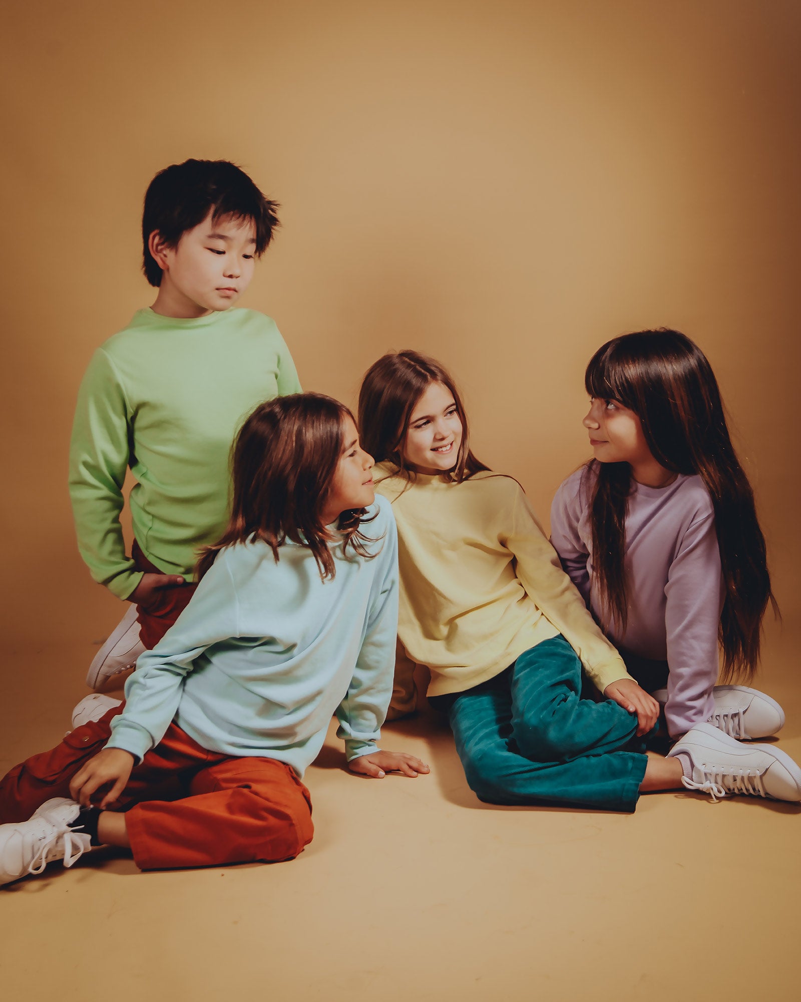 Four children sitting together in a warm studio, wearing colorful Rapozza organic cotton basic long-sleeve tops and pants